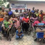 A diverse group of women, some in wheelchairs, poses together outside a building with a banner about empowerment for women with disabilities. They are smiling, creating a positive and supportive atmosphere.