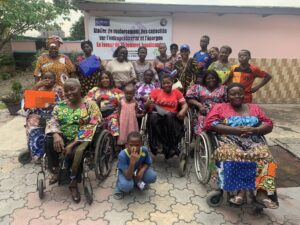A diverse group of women, some in wheelchairs, poses together outside a building with a banner about empowerment for women with disabilities. They are smiling, creating a positive and supportive atmosphere.